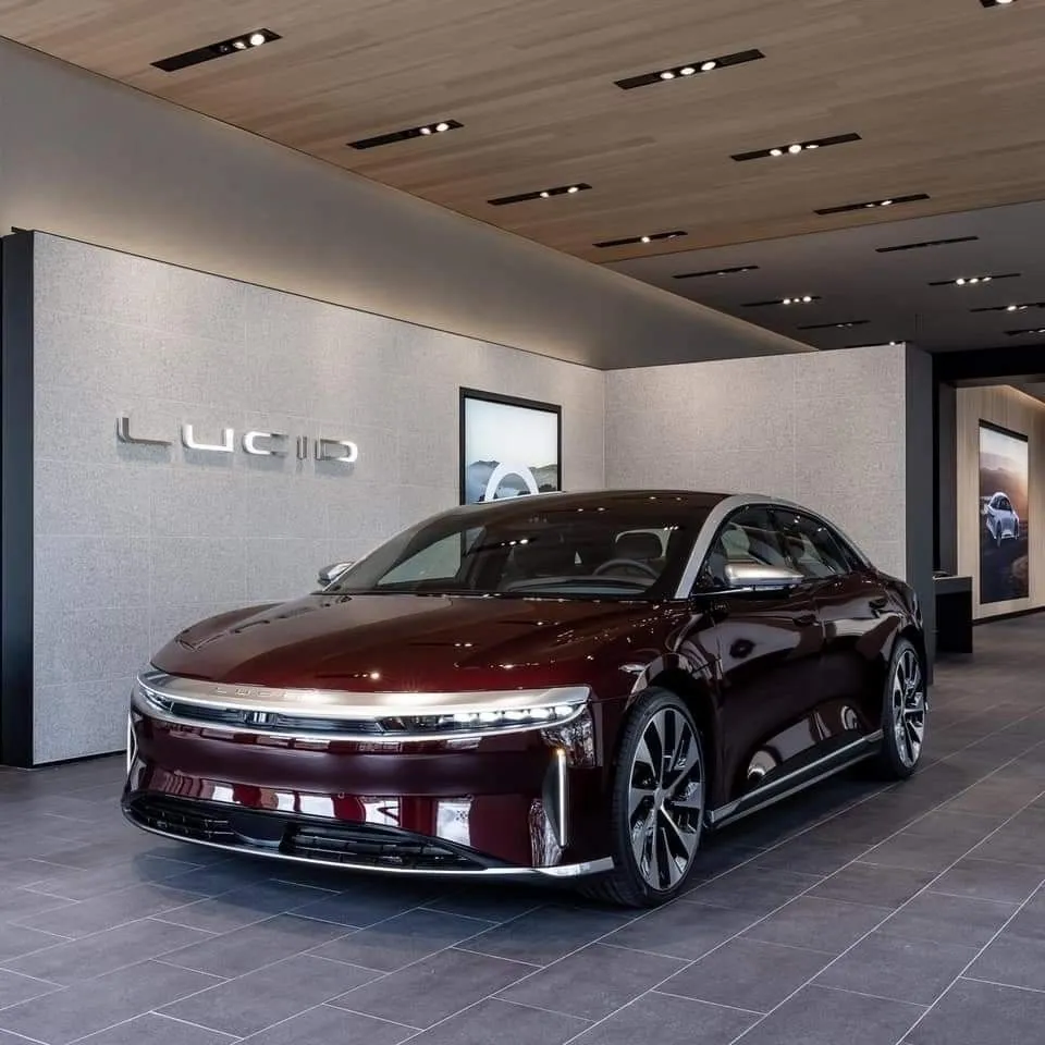 A deep red Lucid sedan under showroom lighting, the Lucid wordmark on the stone wall behind it